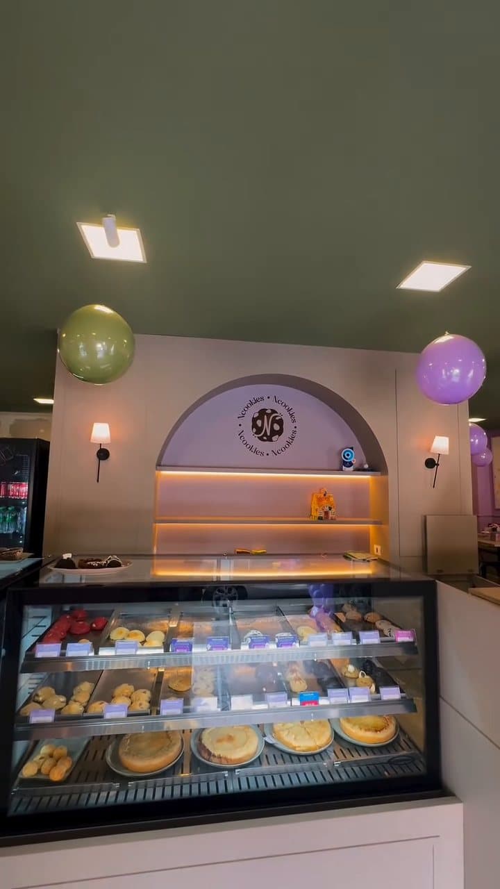 O balcão da Ncookies com o arco lilás, o selo da casa na parede e a vitrine de doces