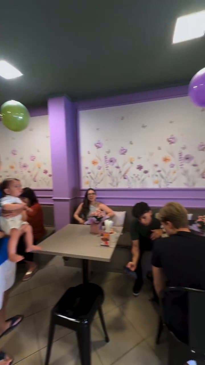 O salão da loja, com a parede lilás, o papel de parede de flores e as mesas cheias