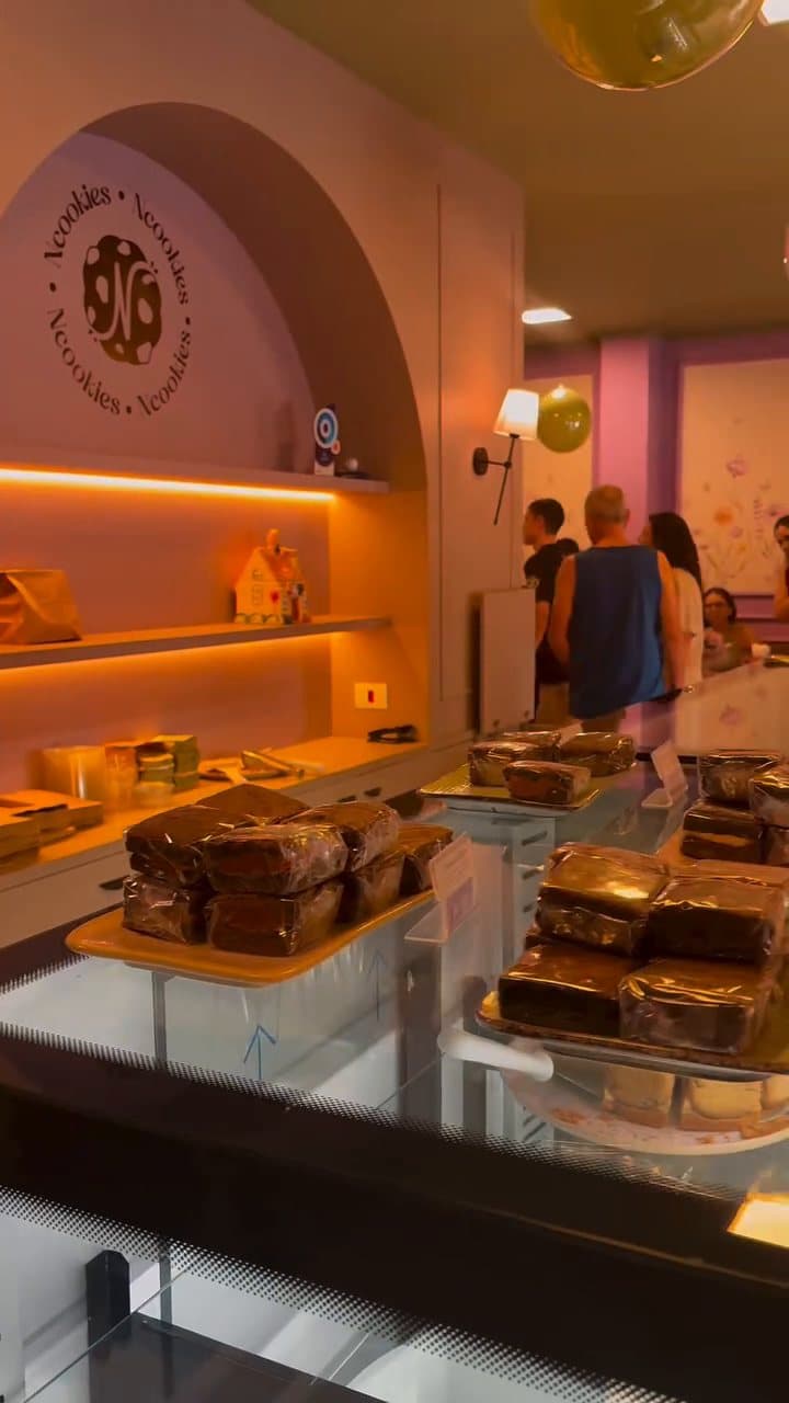 O balcão com bolos e brownies e as prateleiras iluminadas atrás
